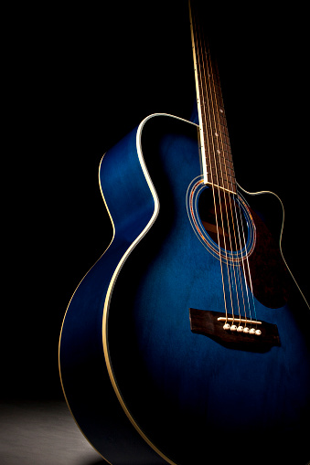 Blue guitar with dramatic lighting fading into a black background.