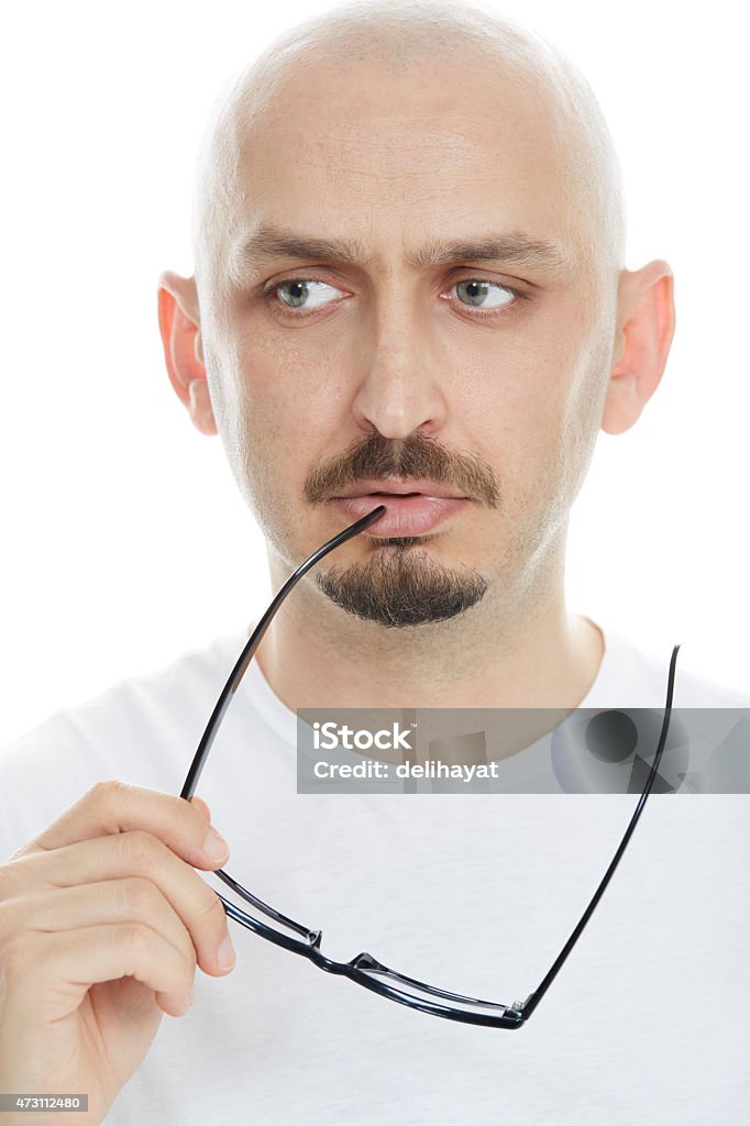 Close-up of a young man thinking with worried expression Close-up of a young man thinking with worried expression and holding eyeglasses 2015 Stock Photo