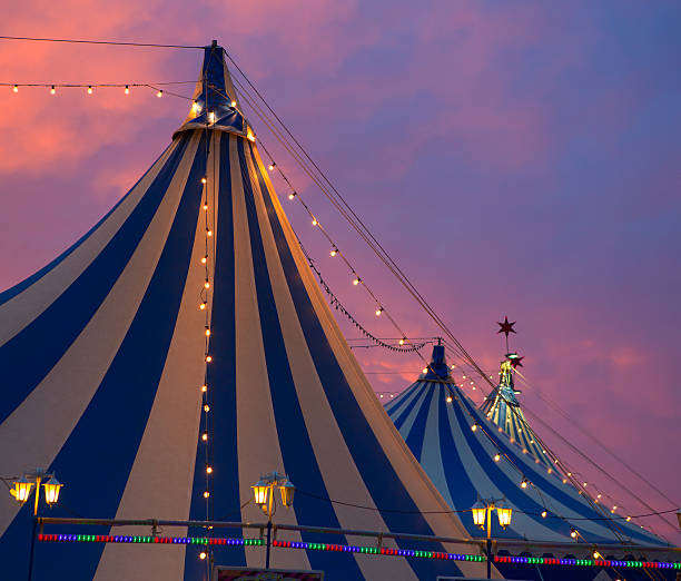 Circus tents illuminated by string lights against sunset