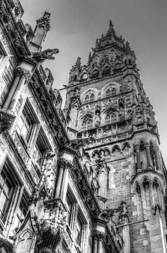 Black and white rendition of the New Town Hall in Marienplatz in downtown Munich, Germany.  The building hosts the city’s government including the city council, officers of the mayors and city administration.  The structure was built between 1867 and 1908.  The building’s main façade is richly-decorated with statues, a large clock tower and other features--and includes the Glockenspiel performed on an apparatus daily.