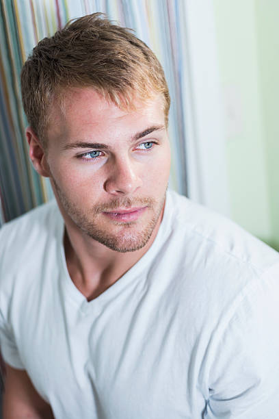 Portrait of young man with hazel eyes Portrait of a handsome young man with hazel eyes, and stubble on his face, looking away from the camera with a serious expression. He has a muscular build and broad chest under his white undershirt. hazel blue eyes stock pictures, royalty-free photos & images