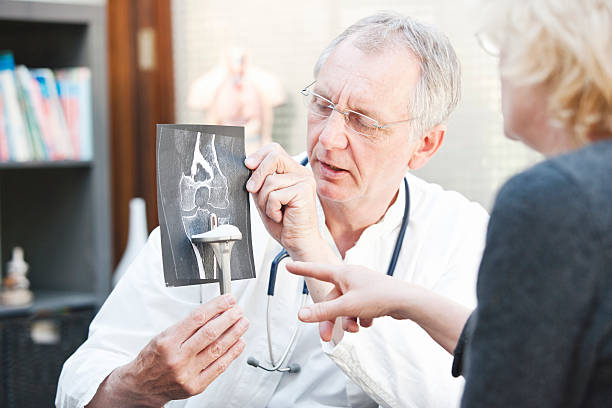 Mature doctor presenting x-ray and knee arthroplasty to female patient A mature medicine presenting a total knee arthroplasty and x-ray to a female patient. This is a so called duohead prosthesis. tibia photos stock pictures, royalty-free photos & images