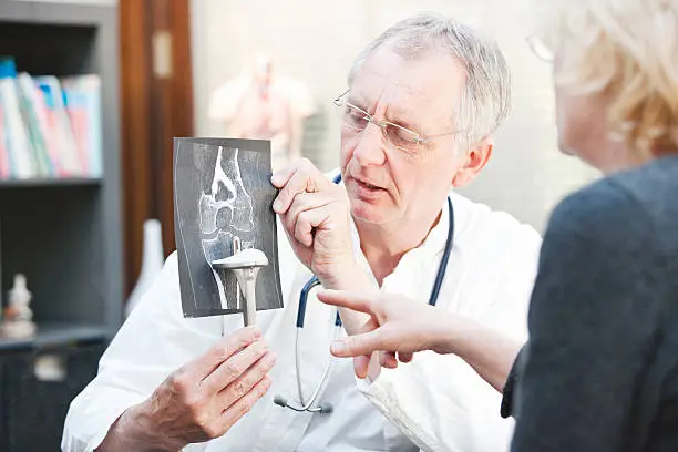 Photo of Mature doctor presenting x-ray and knee arthroplasty to female patient