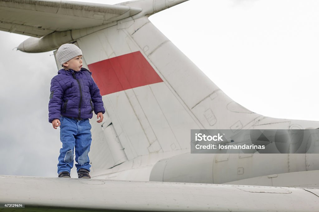 Child on the wing of a jet plane Two years old kid standing on the wing of an old jet plane with red flag on the tail of the plane. 2015 Stock Photo