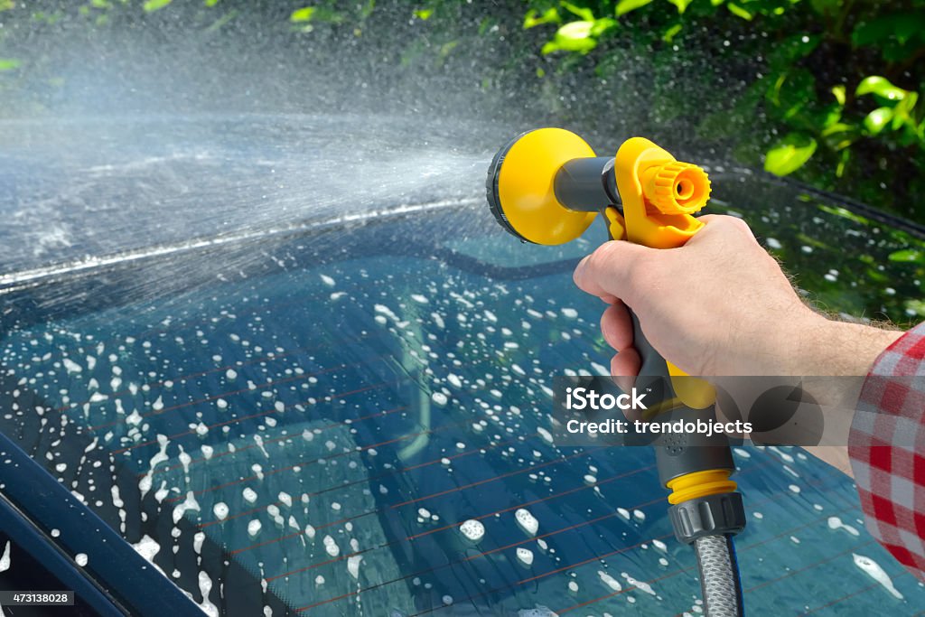 Car Care - washing and rinsing Man washing a car using a garden spray gun 2015 Stock Photo