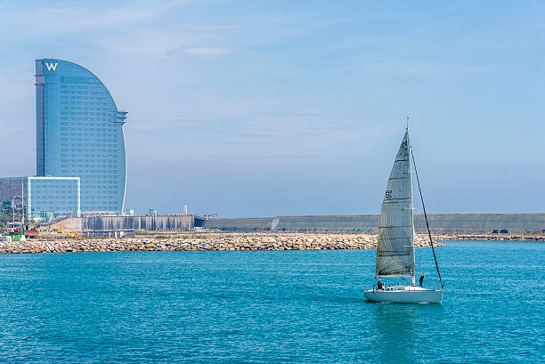 Barcelona, Spain - May 2, 2015: Sailboat sailing out of the harbor with the W hotel designed by Ricardo Bofill in the background