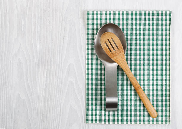 Traditional wooden spoon in stainless steel spoon rest with striped cloth napkin on white wood. Format in horizontal layout.