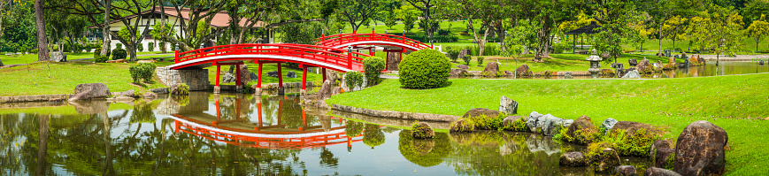 Vibrant red traditional wooden bridge reflecting in the tranquil ponds of the Japanese Gardens park of Singapore. ProPhoto RGB profile for maximum color fidelity and gamut.