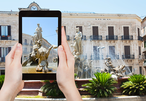 travel concept - tourist takes picture of fountain on Piazza Archimede in Syracuse, Sicily, Italy on tablet pc