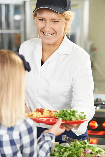 Pupil In School Cafeteria Being Served Lunch By Dinner Lady Pupil In School Cafeteria Being Served Lunch By Dinner Lady cafeteria worker photos stock pictures, royalty-free photos & images