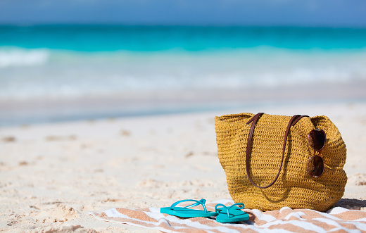 Beach vacation close up. Straw bag, sun glasses, towel and flip flops on a tropical beach