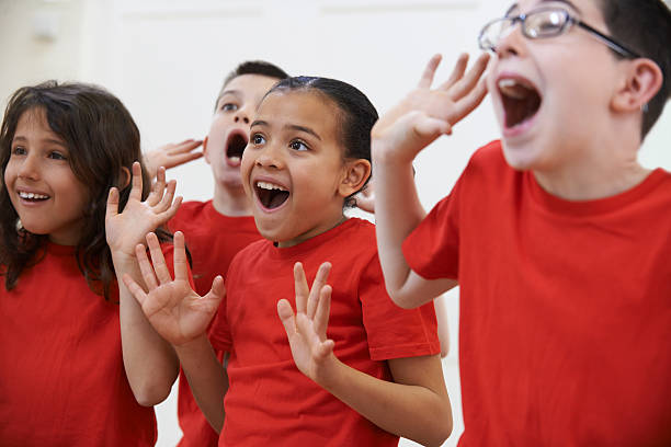 Group of kids in red shirts dramatically acting in drama Group Of Children Enjoying Drama Class Together acting performance stock pictures, royalty-free photos & images