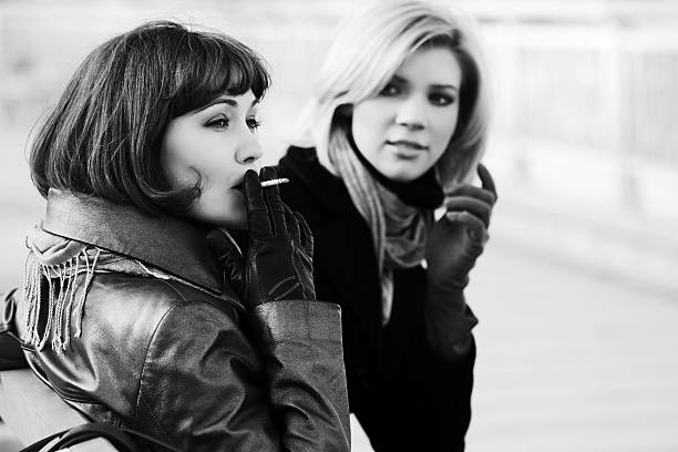 Two happy young fashion women smoking on the bench stock photo