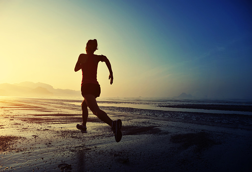 young fitness woman running on sunrise beach