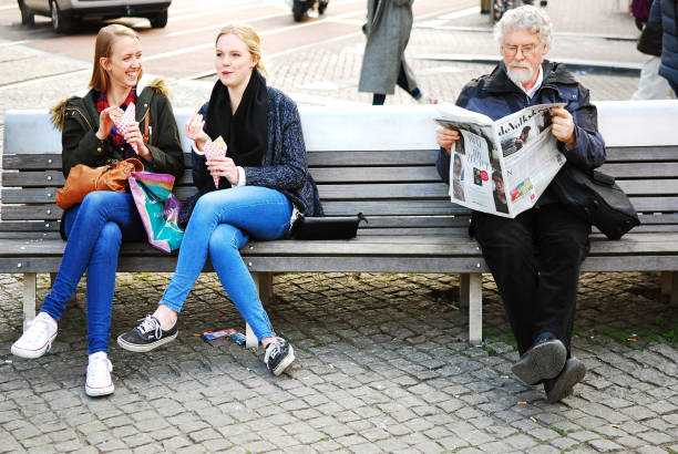 Two friends enjoying a relaxing morning on colorful benches in an outdoor seating area with trees and buildings in the background.
