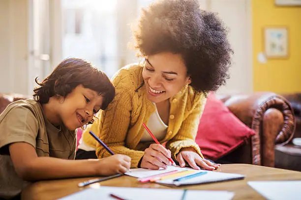 Young happy African American mother having fun with his son at home while coloring together.