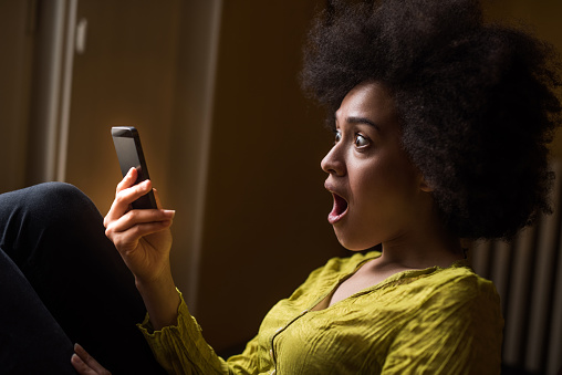 Shocked African American woman reading a text message on mobile phone.