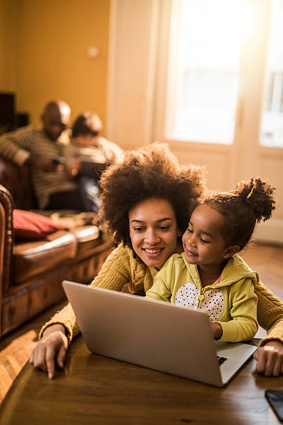 giovane madre afro-americana e figlia usando il portatile a casa. - computer child family laptop foto e immagini stock