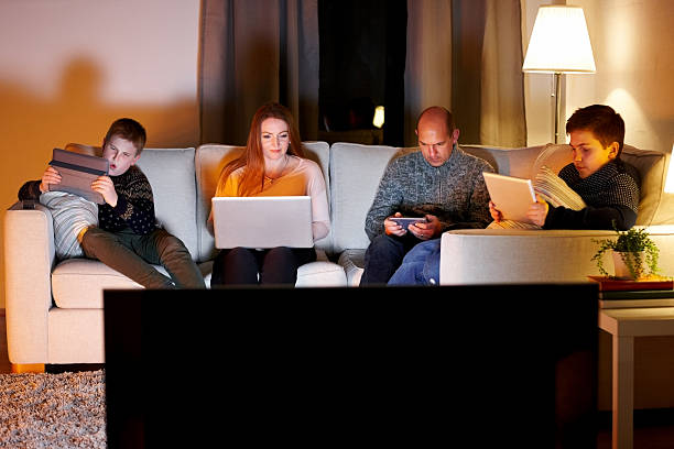 istock Family of four sitting on couch using digital devices 473193898