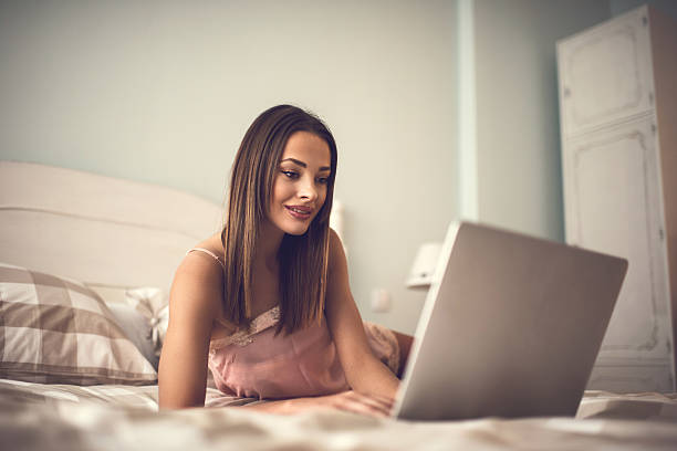 istock Young smiling woman lying on bed and typing on computer. 473206264