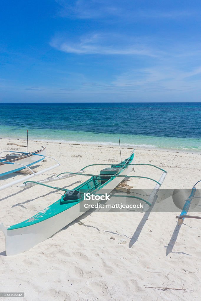 Tropical beach paradise Calm and peaceful sea and beach scene in the Philippines, East Asia. The image has been taken from white sandy beach looking towards the sea. The water is crystal clear and laps gently against the golden sand creating small white waves. The water gradually turns from turquoise to dark blue as it reaches the horizon. On the beach are some traditional boats. 2015 Stock Photo