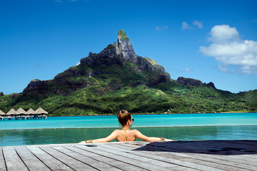 lady in the infinity pool  on the beach of a luxury vacation resort in the lagoon and looking on the Otemanu mountain on the tropical island of Bora Bora, near Tahiti, French Polynesia, Pacific ocean
