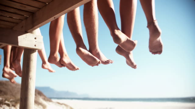 Legs of friends sitting on a beach boardwalk together