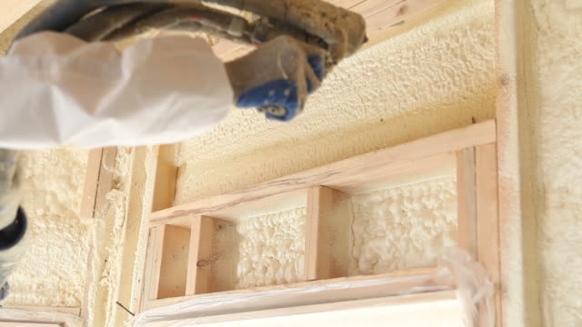 Worker Spraying Expandable Foam Insulation Between Wall Studs