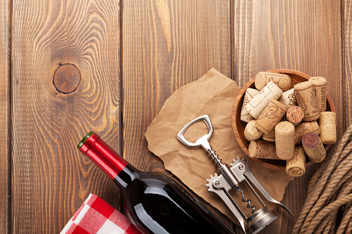 Red wine bottle, corks and corkscrew over wooden table background. Top view with copy space