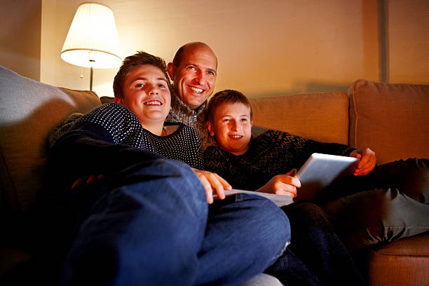 istock Happy father and sons relaxing on sofa with digital tablet 473233826