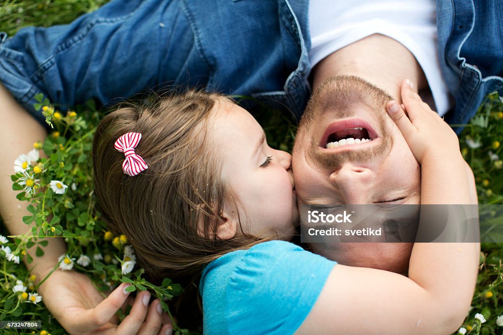 Father and daughter outdoors in a meadow. Father and his cute daughter having fun outdoors in a meadow. Lying on green grass and daisy flowers, embracing. Caucasian, blond hair. Father's Day Stock Photo