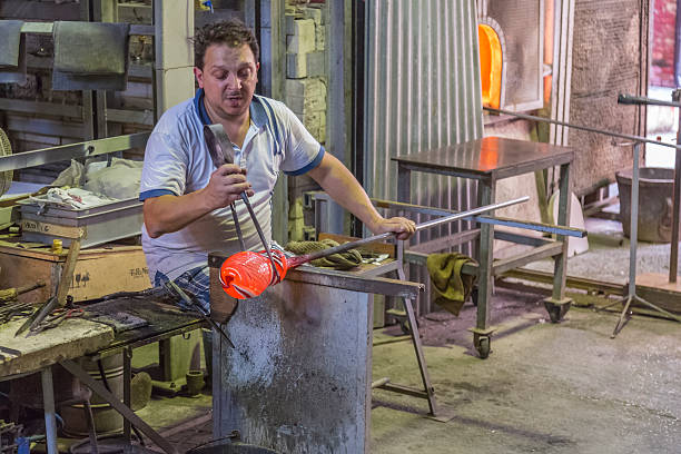 Murano, Italy - October 2, 2014: Glass Blower at work in Murano factory , Italy.  We see a glassblower at work creating a glass vase. This artist works in a workshop that allows tourists to witness the manufacture of some glass pieces and photos are permitted during this session. Then, tourists can buy glasses of the related parts shop in the workshop.