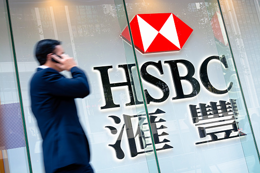 Hong Kong, Hong Kong SAR -November 17, 2014: Motion blured business man passing by an HSBC Bank sign in Hong Kong. HSBC Holdings plc  is the world's third largest bank by assets.