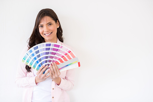 Happy woman painting a wall in her house and holding a color swatch