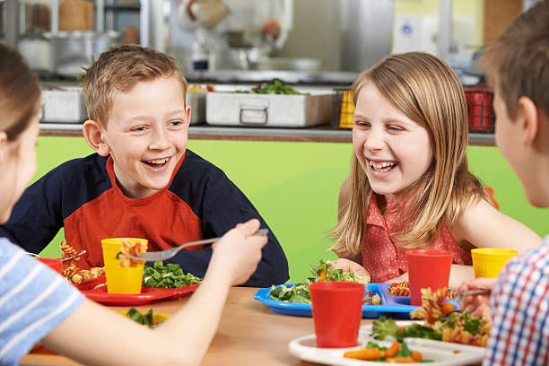 studenti seduti al tavolo a scuola caffetteria mangiare pasto - child food school children eating foto e immagini stock