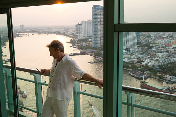 istock Man texts from hotel railing, above city, river 473297080