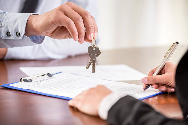 Handing over keys when signing contract Young woman is signing financial contract with male Real Estate Agent. Close-up. estate agent sign stock pictures, royalty-free photos & images