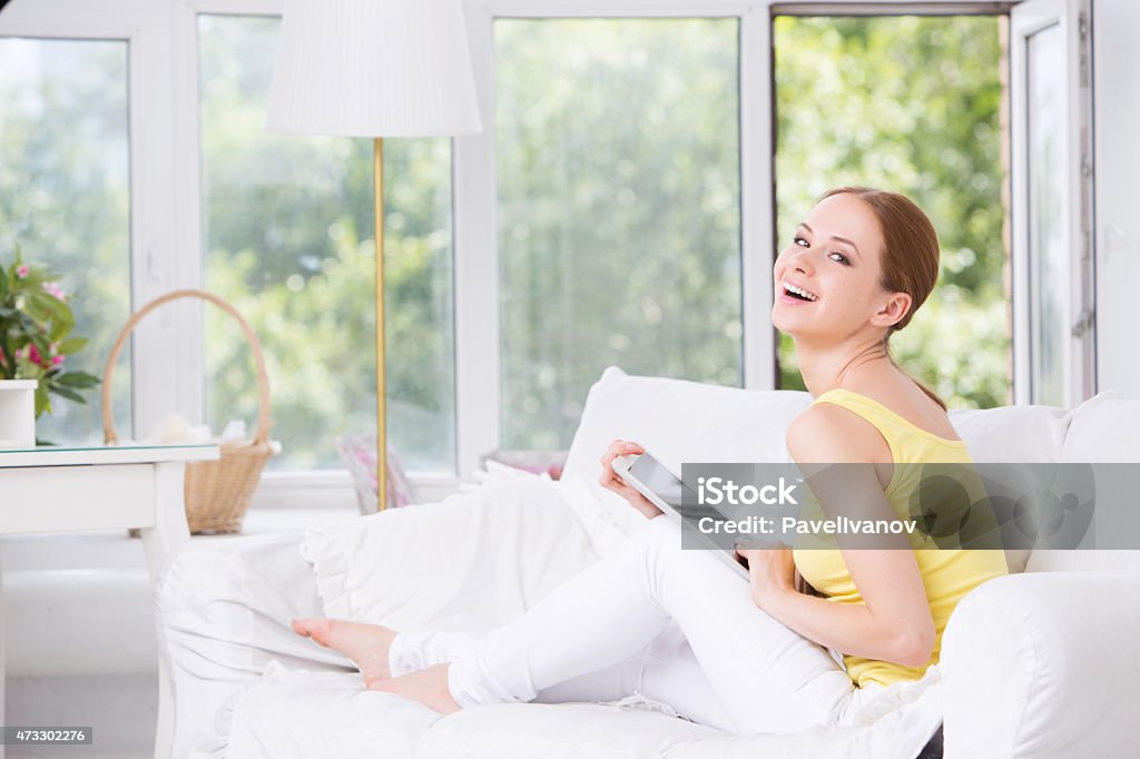 Young beautiful girl sitting on the couch and shows touchpad 2015 Stock Photo