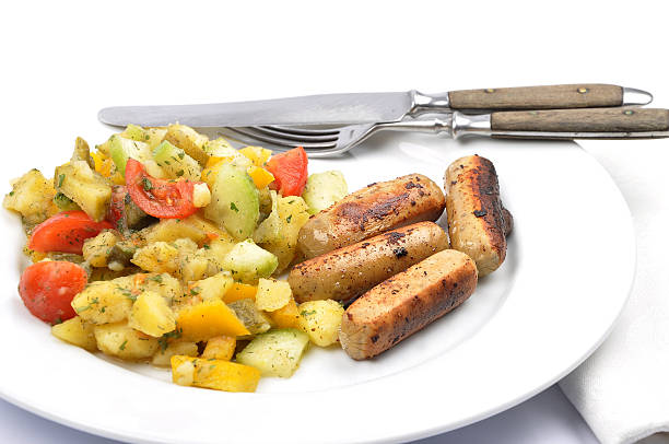 Homemade dinner plate with grilled sausages, roasted potatoes, and fresh salad with cherry tomatoes and olives. Represents hearty meal, comfort food, and colorful home cooking concept