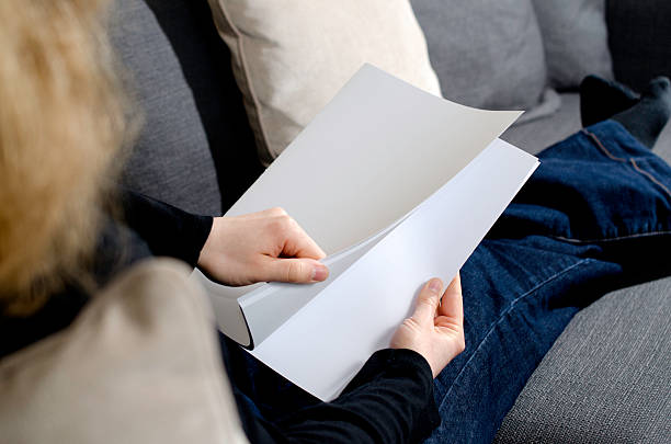 istock Woman lying on sofa opening a blank white brochure 473307672