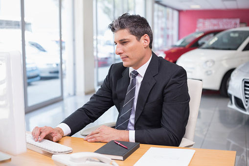 Focused businessman using his laptop at new car showroom