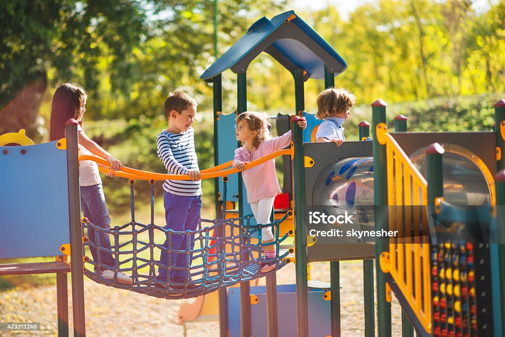 Children playing in the park at playground and communicating. Small group of children having good time at jungle gym and talking. Playground Stock Photo