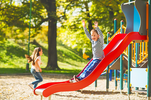 Little boy having fun while sliding with his hands raised. There are children in the background.