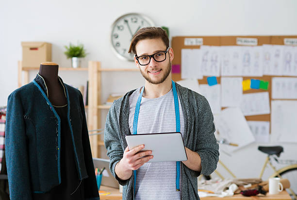 Fashion designers Young man fashion designer using digital tablet at office business person one man only blue standing stock pictures, royalty-free photos & images