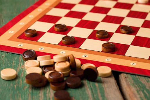 Horizontal photo of Heap of wooden stones for Game of checkers. Heap is on wooden board with green worn color in front of paper board for game with few stones on