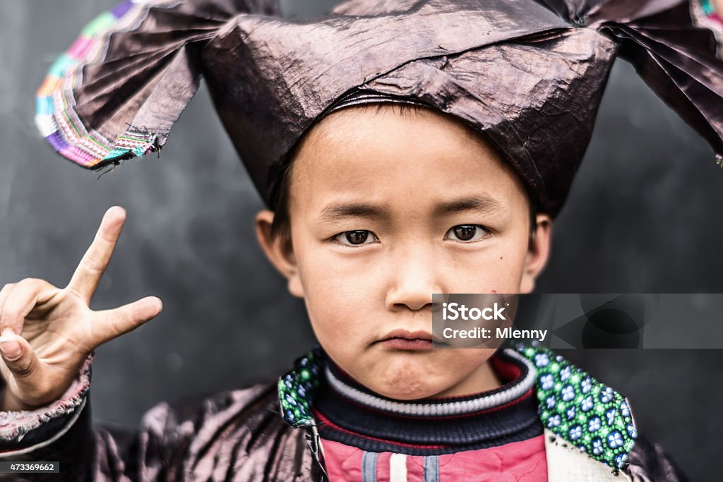 Chinese Boy in Traditional Dong Clothing Facial Portrait of a Chinese schoolboy, wearing the traditional clothing of the Dong people. The boy is posing with peace sign, keeping serious eye contact. Huang Gang, small Dong Village in Guizhou, China. Child Stock Photo