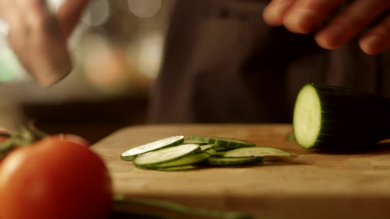 Szef kuchni kroi ogórek nożem na desce do krojenia, kładąc nacisk na precyzyjne cięcie w kuchni molekularnej.