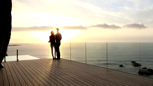 Couple watching sunset from luxury patio overlooking ocean