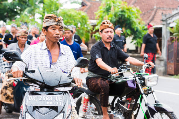 Temukus, Indonesia - January 23, 2015: In rural Northern Bali men wearing traditional clothing drive on motorbikes as part of a funeral procession ceremony.