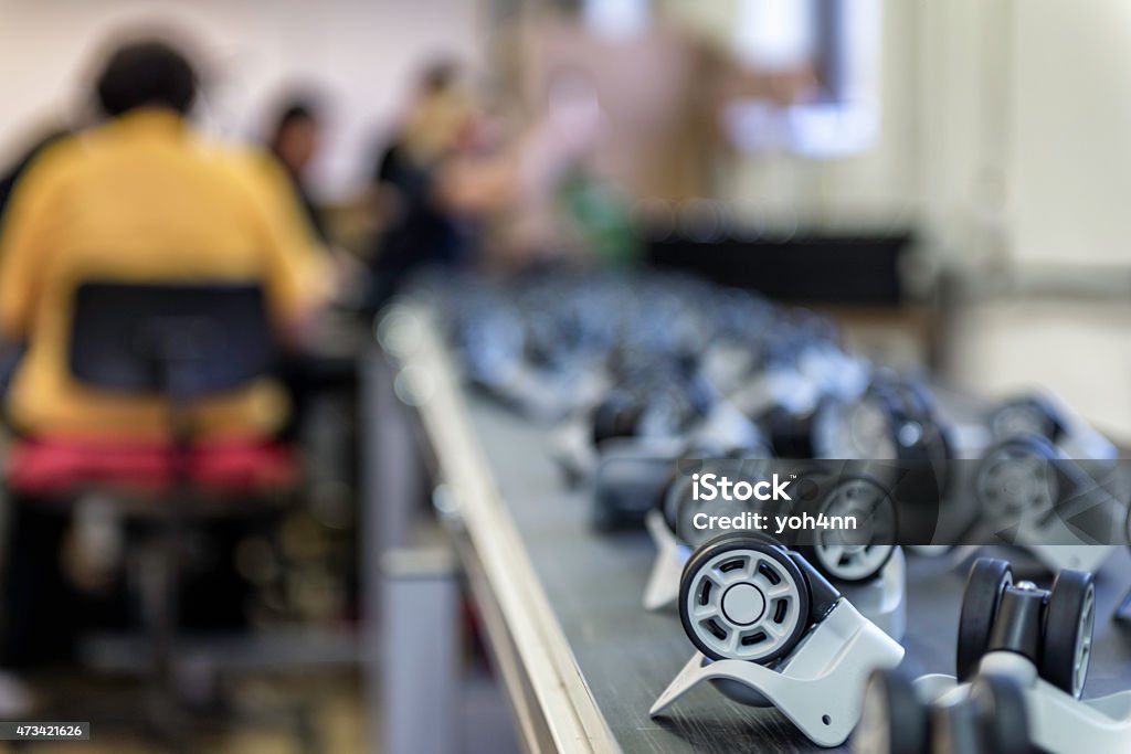 Conveyor belt with plastic wheel Automated line in factory with plastic pieces, people in background. In A Row Stock Photo